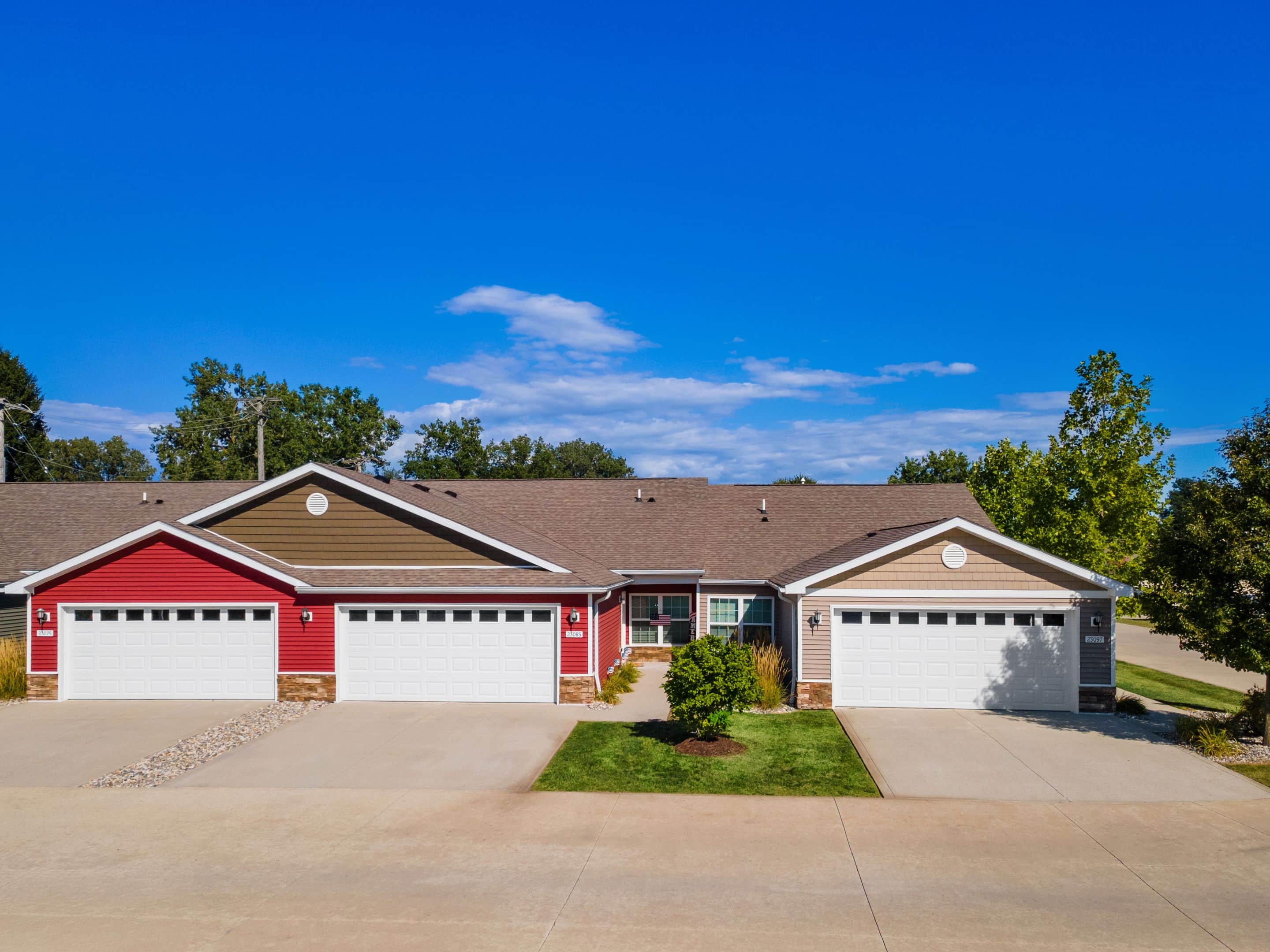 A row of single-story townhouses with attached double garages, red and beige siding, and a clear blue sky overhead.