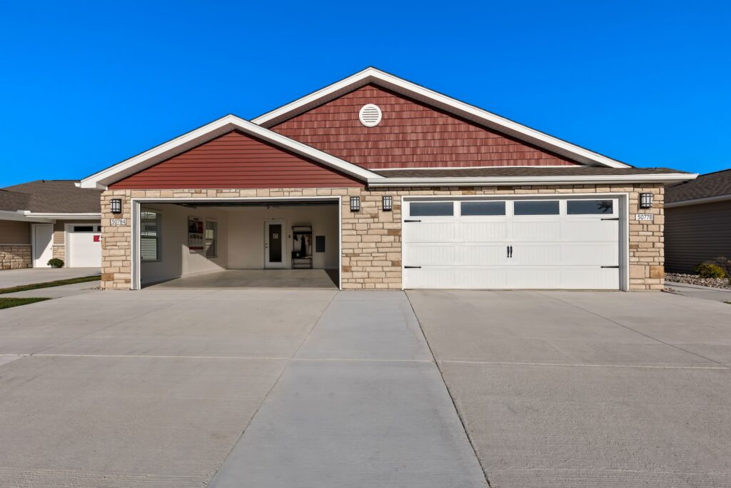 A modern house with a red and tan exterior, featuring a large driveway and a three-car garage with white doors.