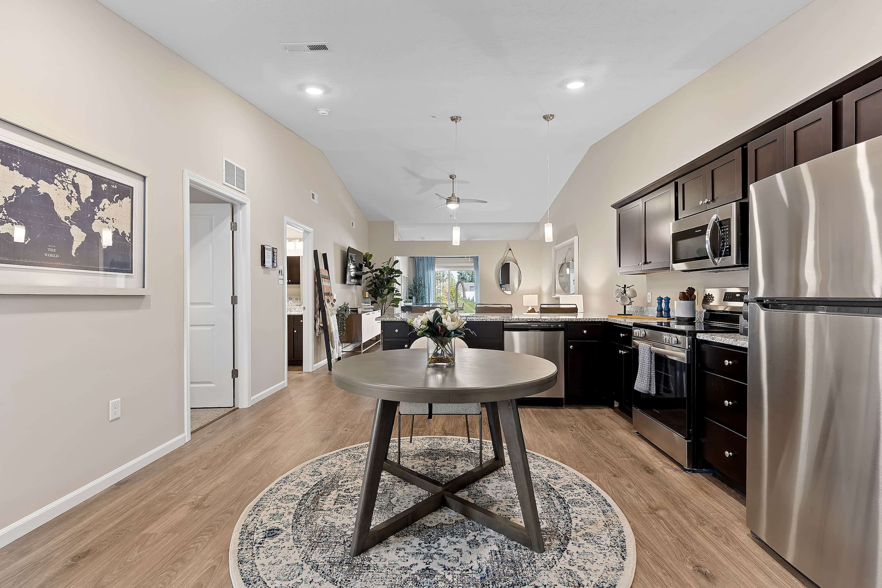 Modern open-concept kitchen and dining area with dark cabinets, stainless steel appliances, round dining table, and light wood flooring.