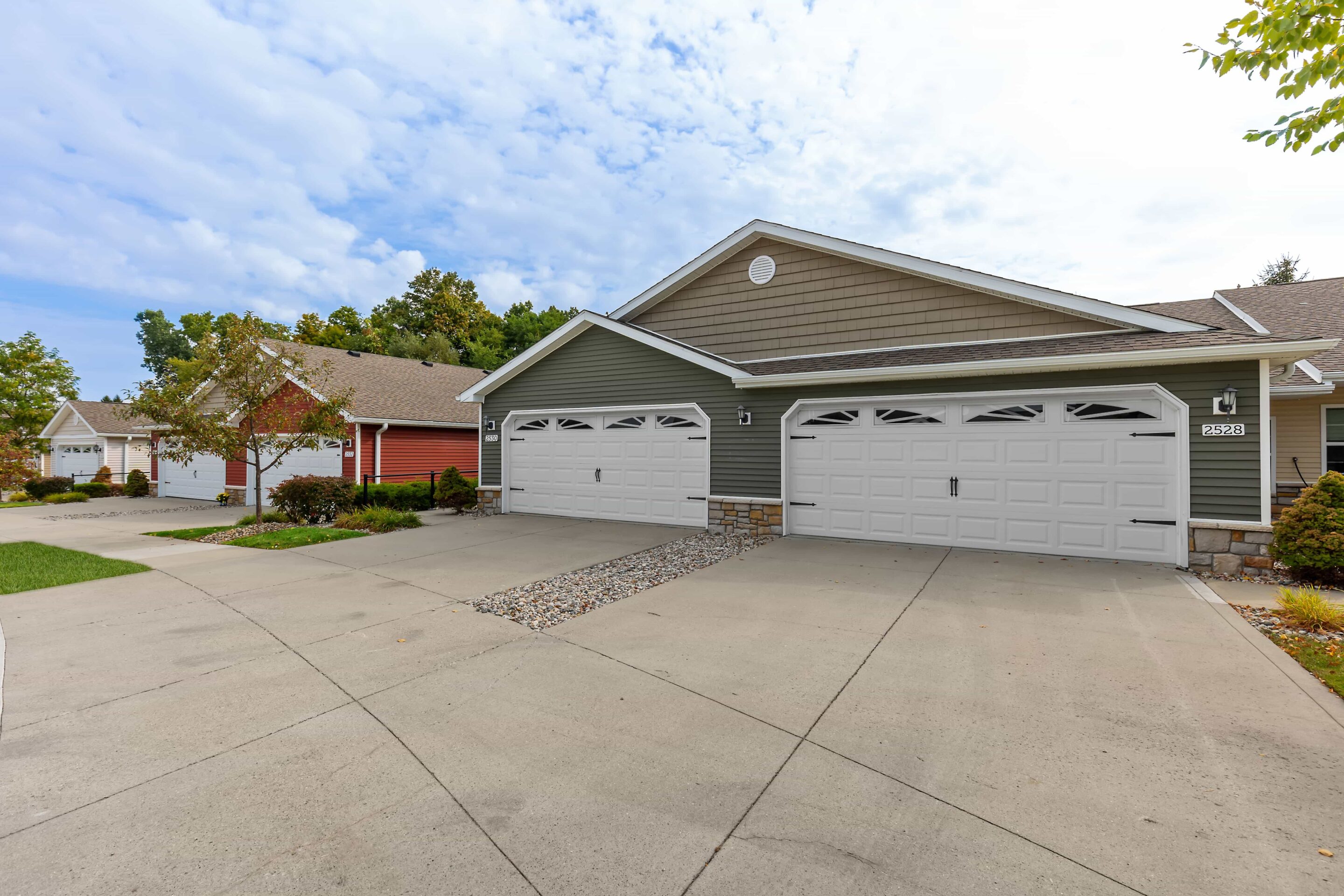 Row of suburban townhouses with attached double garages, stone accents, and neatly maintained driveways under a partly cloudy sky.