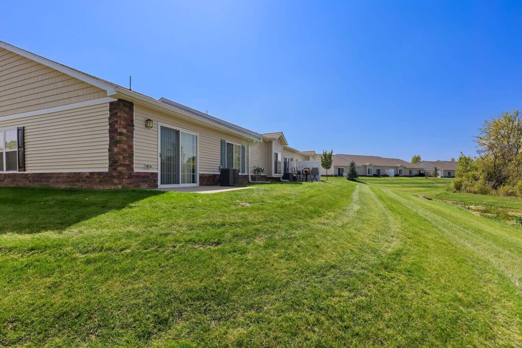 Row of single-story residential buildings with sliding glass doors opening onto well-maintained grassy backyards on a clear, sunny day.