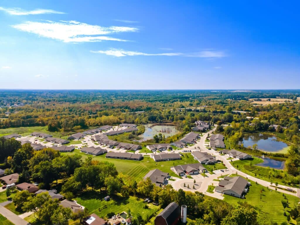 Aerial view of a suburban residential neighborhood with curved streets, single-family homes, ponds, and abundant greenery under a clear blue sky.