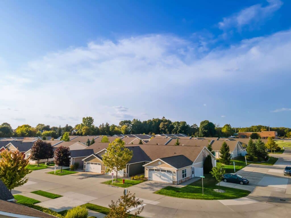A suburban neighborhood with rows of single-story houses, lawns, trees, and driveways on a clear, sunny day.