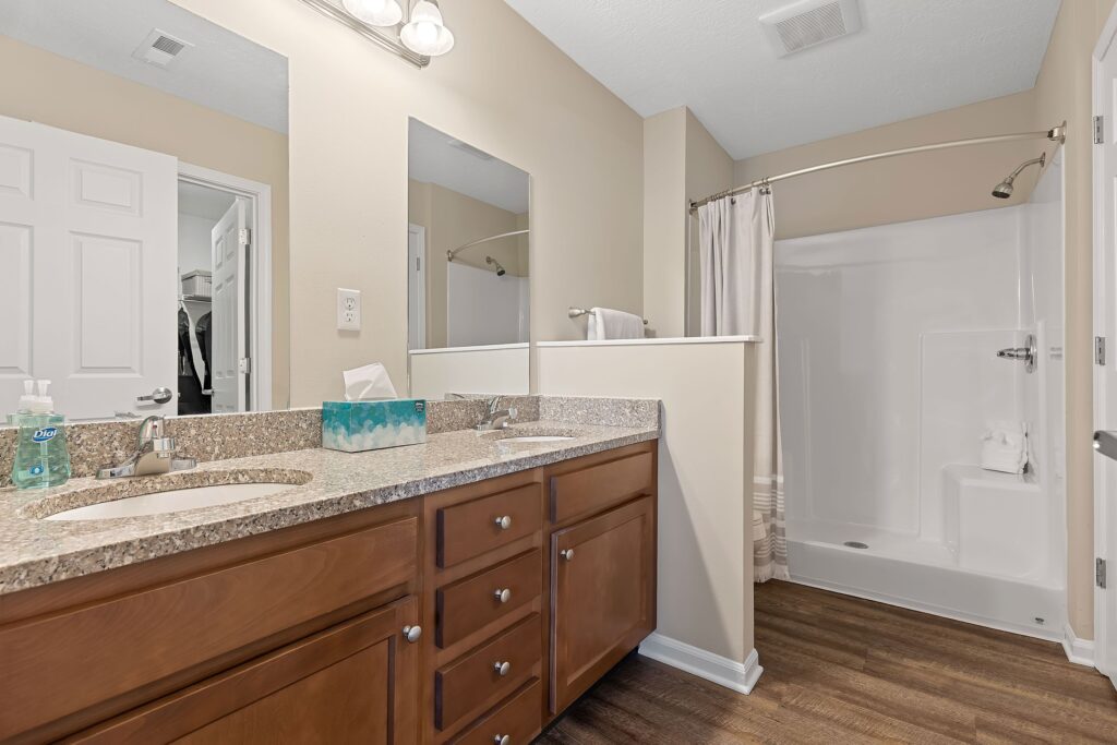 Bathroom with a double-sink vanity, granite countertop, wooden cabinets, large mirror, and a walk-in shower with a curtain.