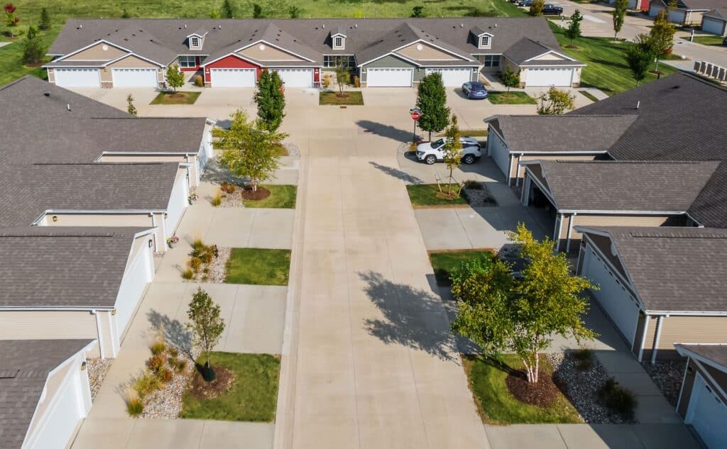 Aerial view of a residential neighborhood with several single-story houses, driveways, garages, parked cars, and landscaped lawns along a central street.