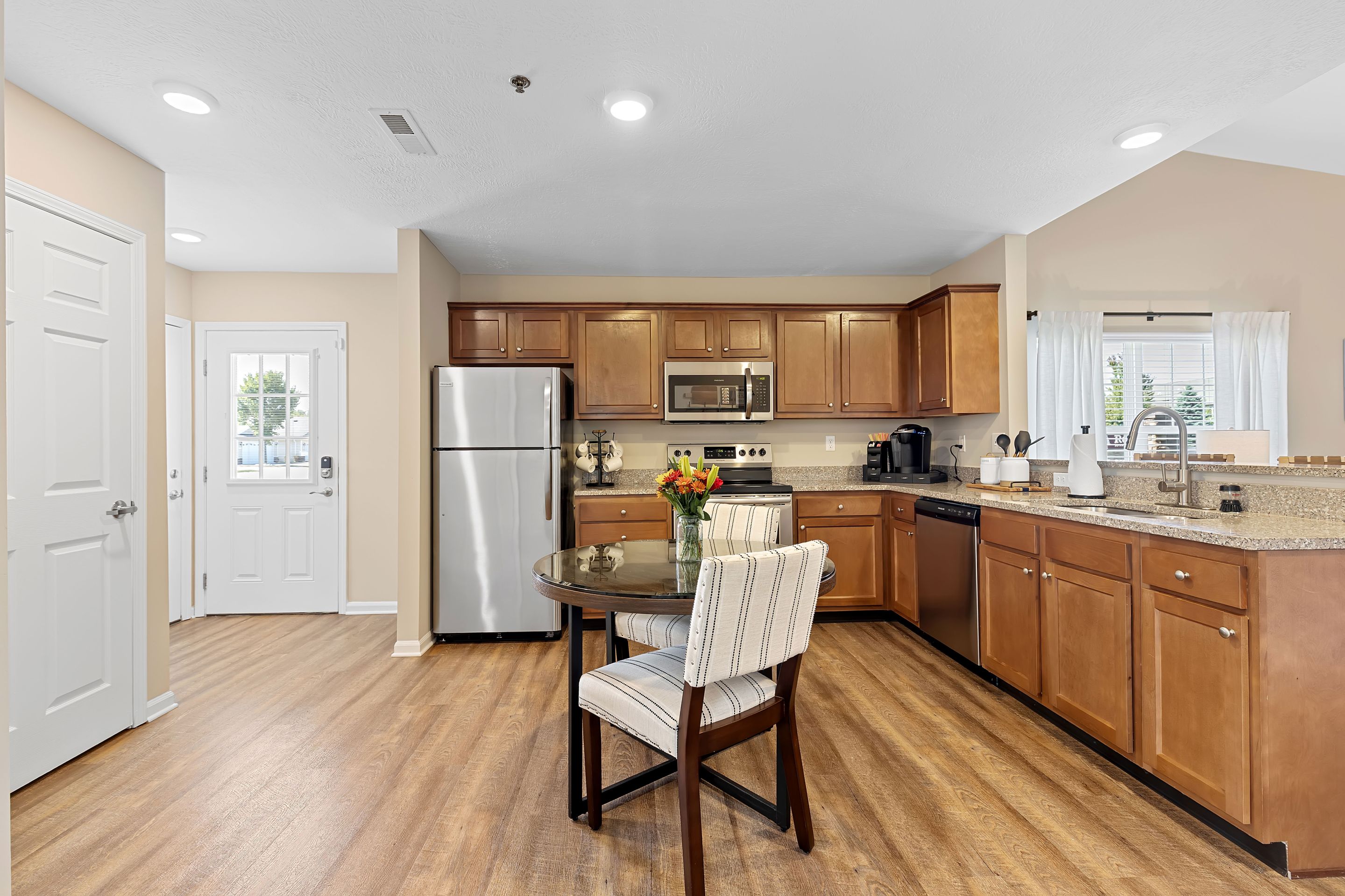 Modern kitchen with wooden cabinets, stainless steel appliances, a round dining table with two chairs, and a vase of flowers on the table.
