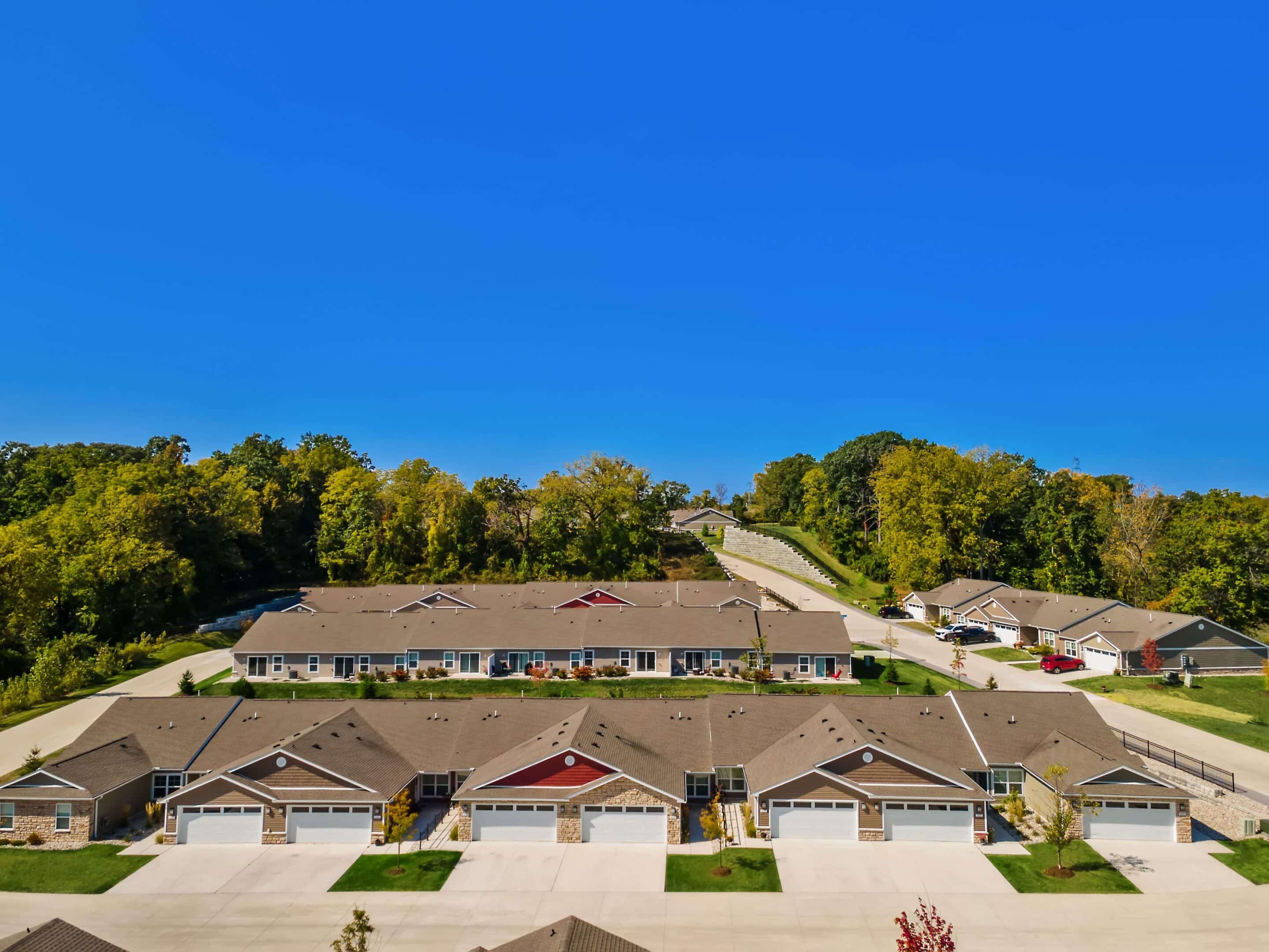 Aerial view of multi-unit residential buildings with attached garages, surrounded by trees and set under a clear blue sky.
