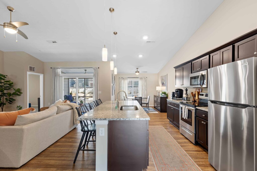 Modern open-concept kitchen and living room with stainless steel appliances, dark wood cabinets, granite countertop, island seating, and neutral decor.