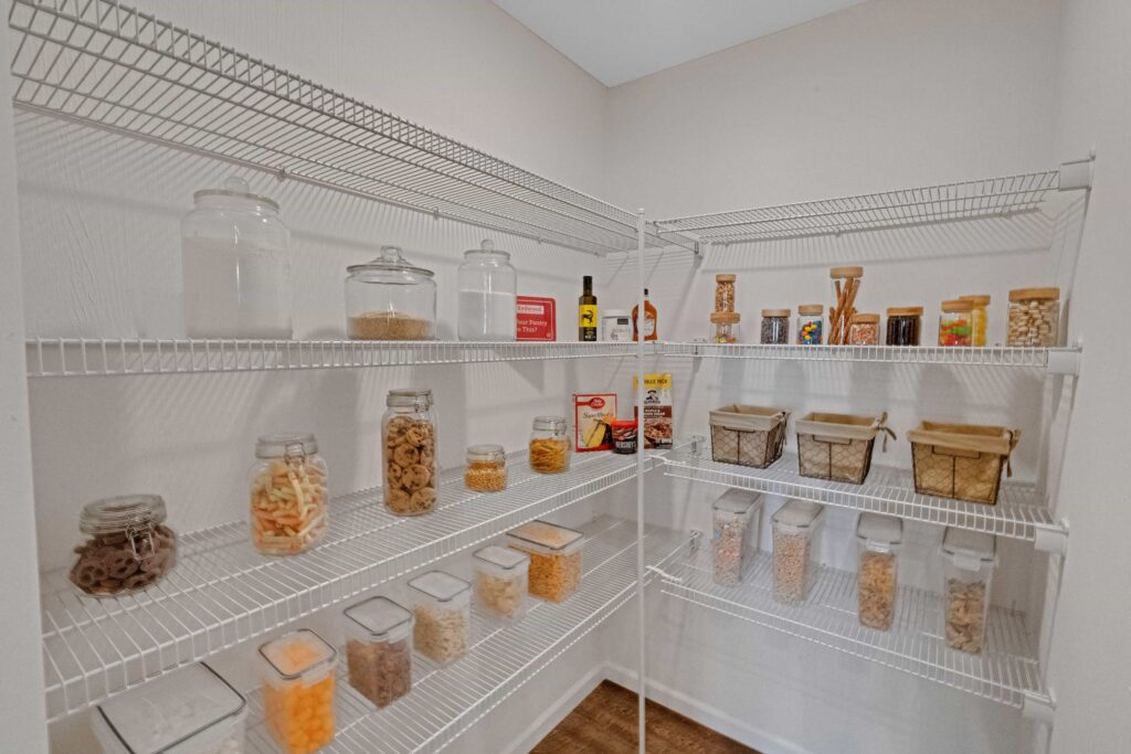 A pantry with white wire shelves holds various clear containers filled with dry goods, jars, baskets, and bottles, all neatly organized.