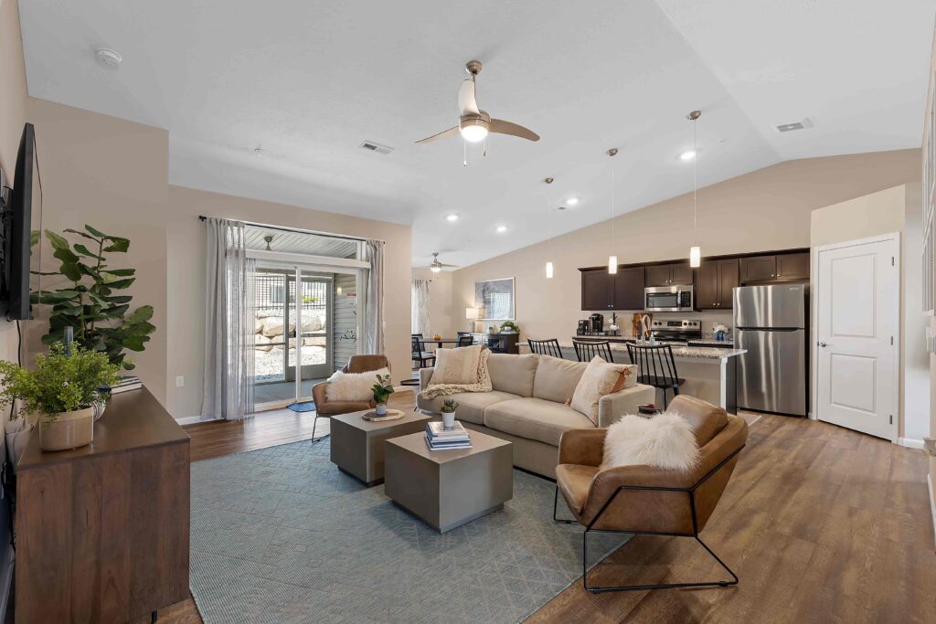 Open-concept living room and kitchen with neutral decor, wood flooring, modern furniture, stainless steel appliances, and sliding doors leading to an outdoor area.