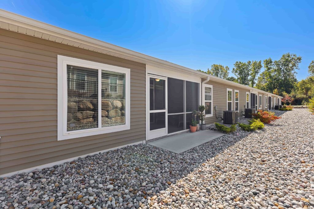A single-story building with beige siding, large windows, a central screened door, and a rocky landscaping area under a clear blue sky.