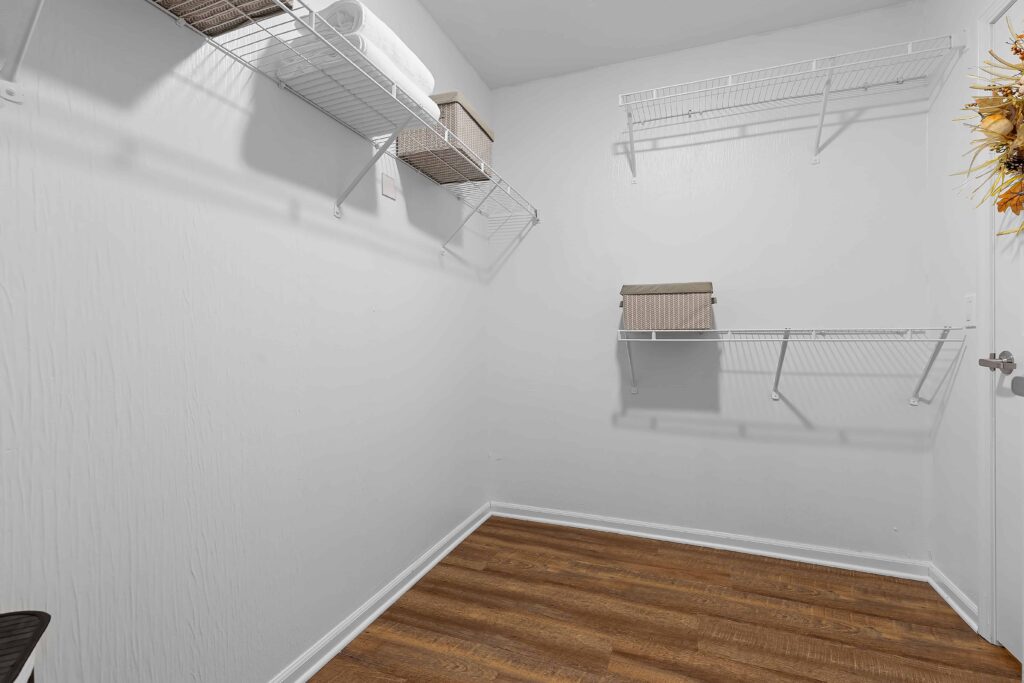 Empty walk-in closet with white wire shelves on the walls, a few storage boxes, and wood-look flooring.