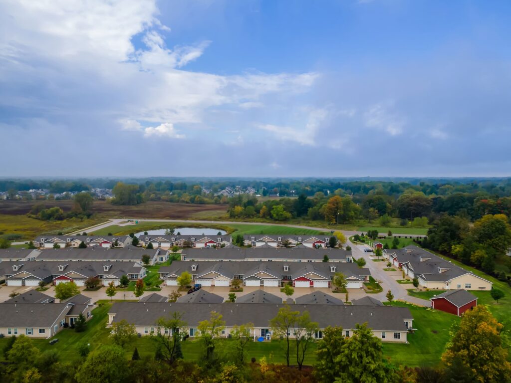 Aerial view of a residential neighborhood with rows of houses, greenery, trees, and an overcast sky in the background.