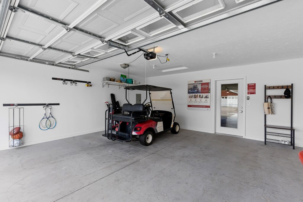 A clean garage with a red golf cart parked inside, sports equipment on wall racks, and a door leading to the interior of the house.