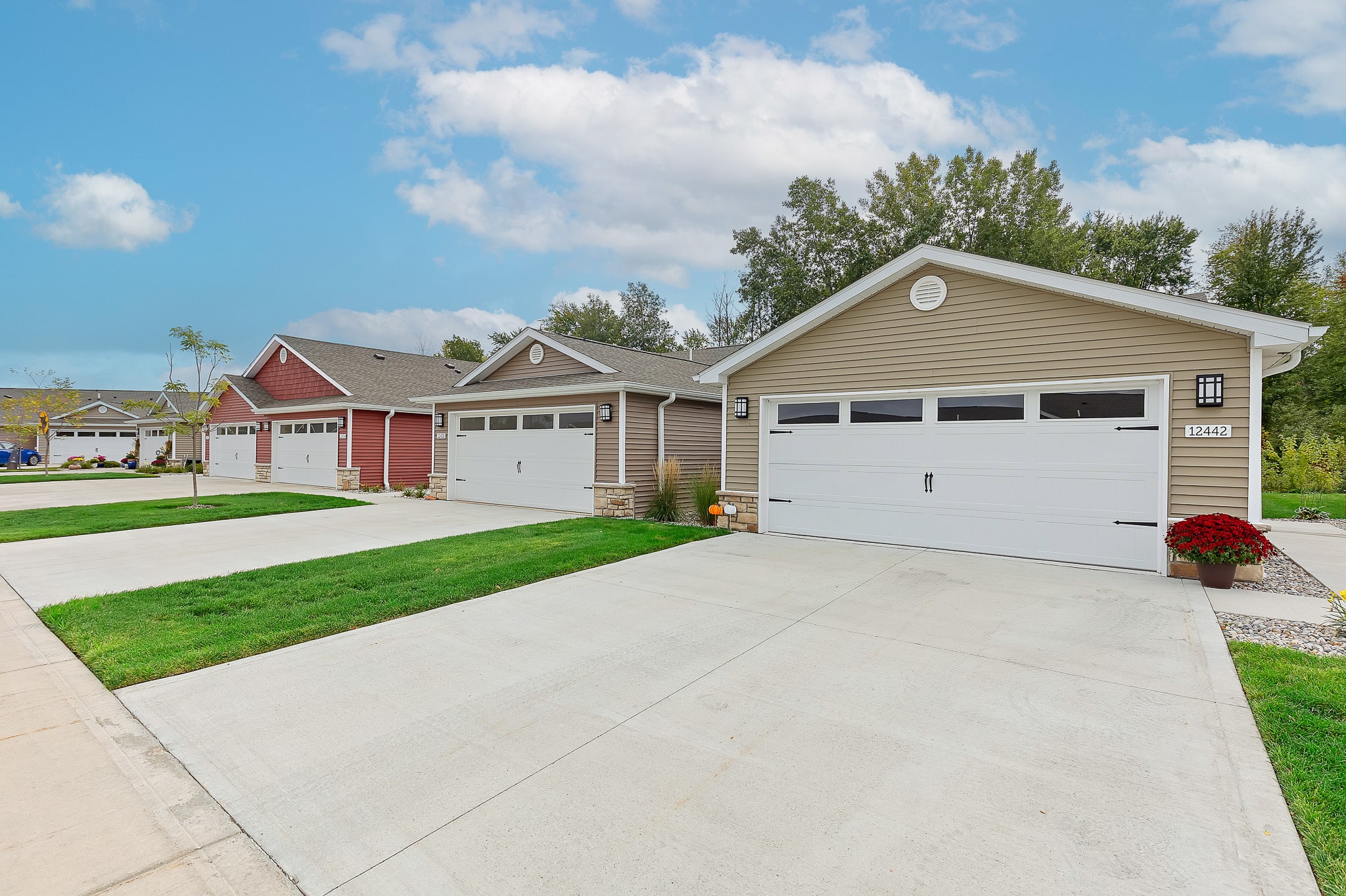 Row of three single-story suburban houses with attached garages, each with a driveway and manicured lawns under a partly cloudy sky.