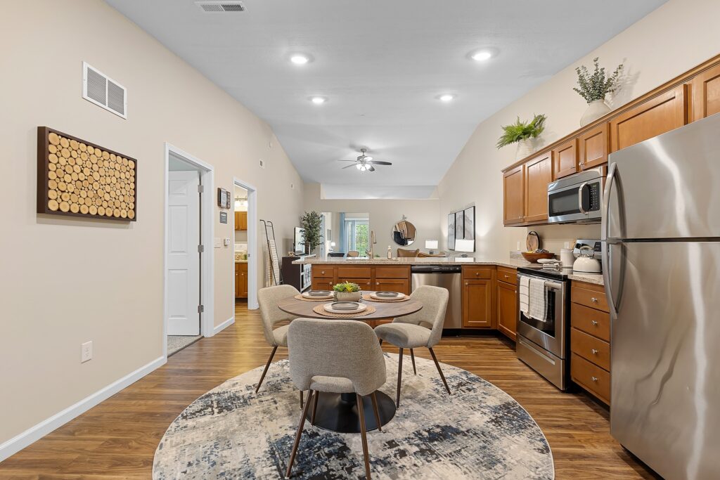 Modern kitchen and dining area with wooden cabinets, stainless steel appliances, a round table with four chairs, and decorative plants on top of cabinets.