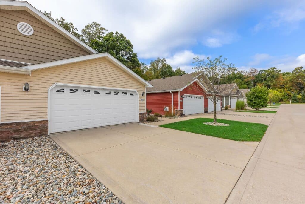 Row of suburban houses with attached garages, concrete driveways, and well-maintained lawns along a quiet residential street.