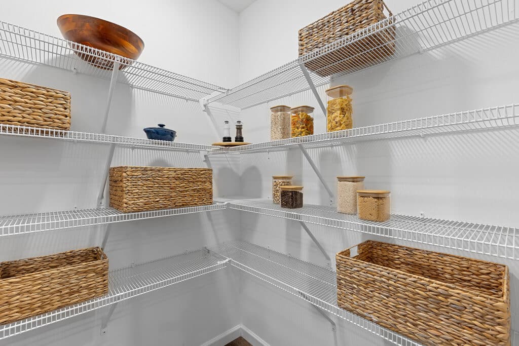 Wire pantry shelves with woven baskets, glass jars containing dry ingredients, a blue dish, and salt and pepper shakers in a well-lit, organized storage space.