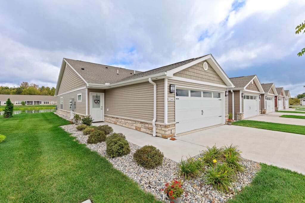 Single-story house with beige siding, a two-car garage, and a small landscaped front yard with shrubs and rocks, situated in a suburban neighborhood.
