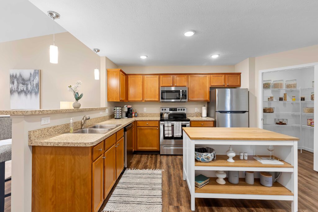 Modern kitchen with wood cabinets, stainless steel appliances, a double sink, granite countertops, island with open shelving, and a walk-in pantry with organized shelves.