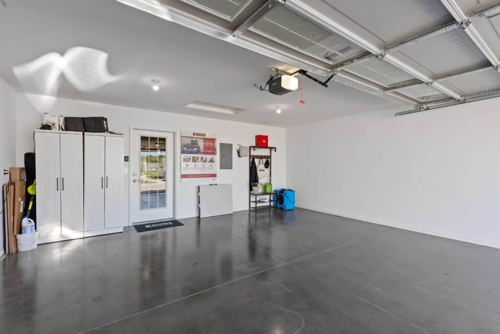 A clean, organized garage with polished concrete floors, white storage cabinets, a metal shelving unit, and an open garage door letting in natural light.