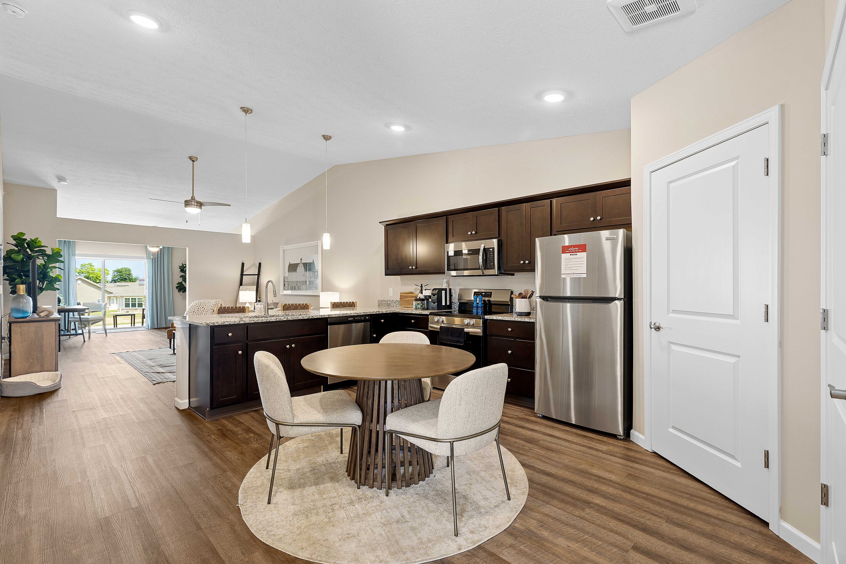 Modern open-concept kitchen and dining area with dark wood cabinets, stainless steel appliances, round table with four chairs, and wood flooring.
