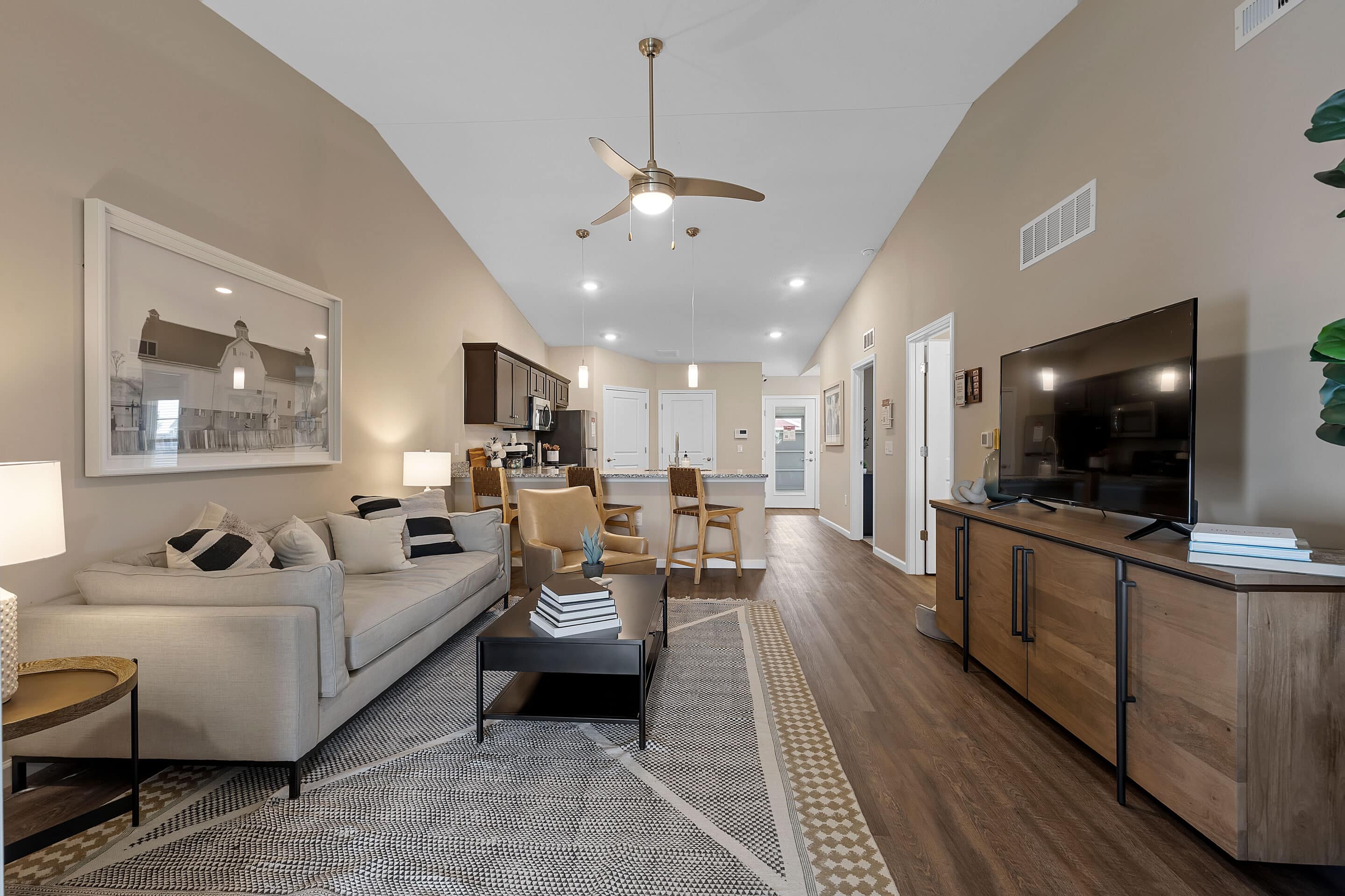 Open-concept living room and kitchen with beige walls, wood flooring, sofa, TV, dining table, modern decor, and ceiling fan.