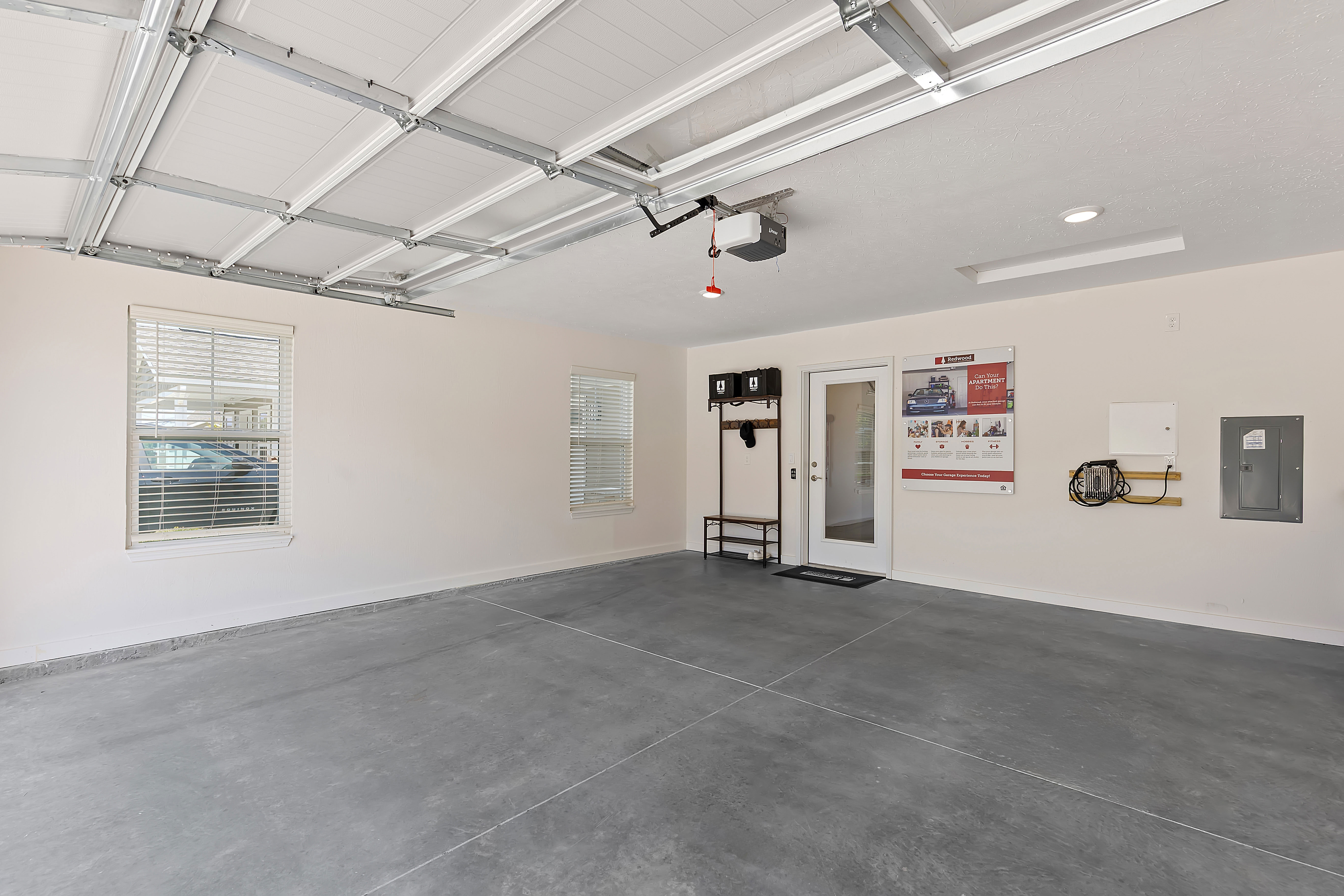 Bright, clean two-car garage with finished walls, gray concrete floor, wall-mounted storage, windows, and a door leading into the house.