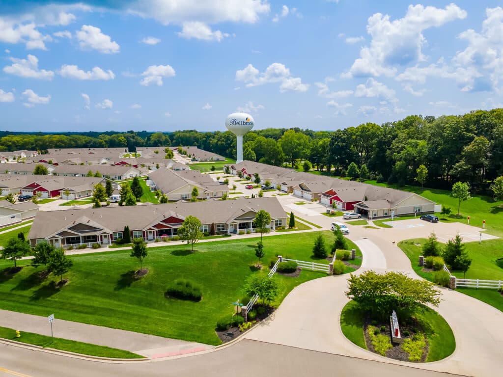 Aerial view of a suburban neighborhood with single-story houses, green lawns, curving roads, and a water tower marked "Belton" in the background.