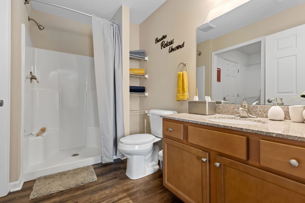 Bathroom with a walk-in shower, toilet, wooden vanity with sink, wall shelves holding towels, and a large mirror above the sink.