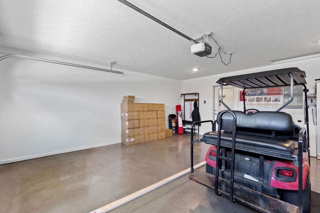 A clean garage with a red golf cart, a stack of cardboard boxes against the wall, and various tools and items on shelves and racks in the background.