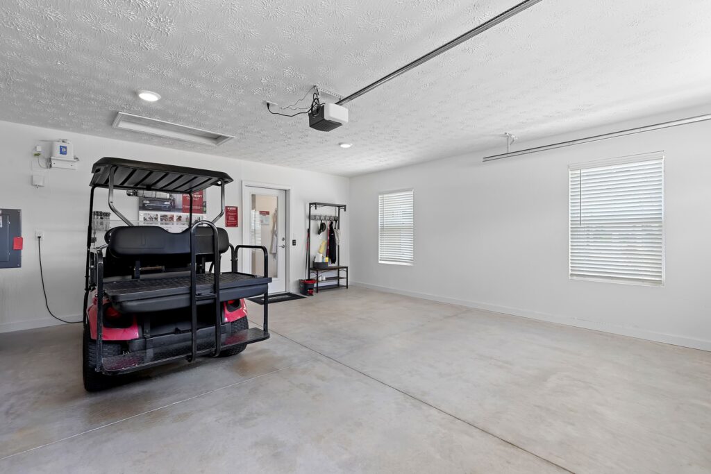 A clean, spacious garage with a golf cart parked on the left, coat rack and shelves near the back wall, and two windows letting in natural light.