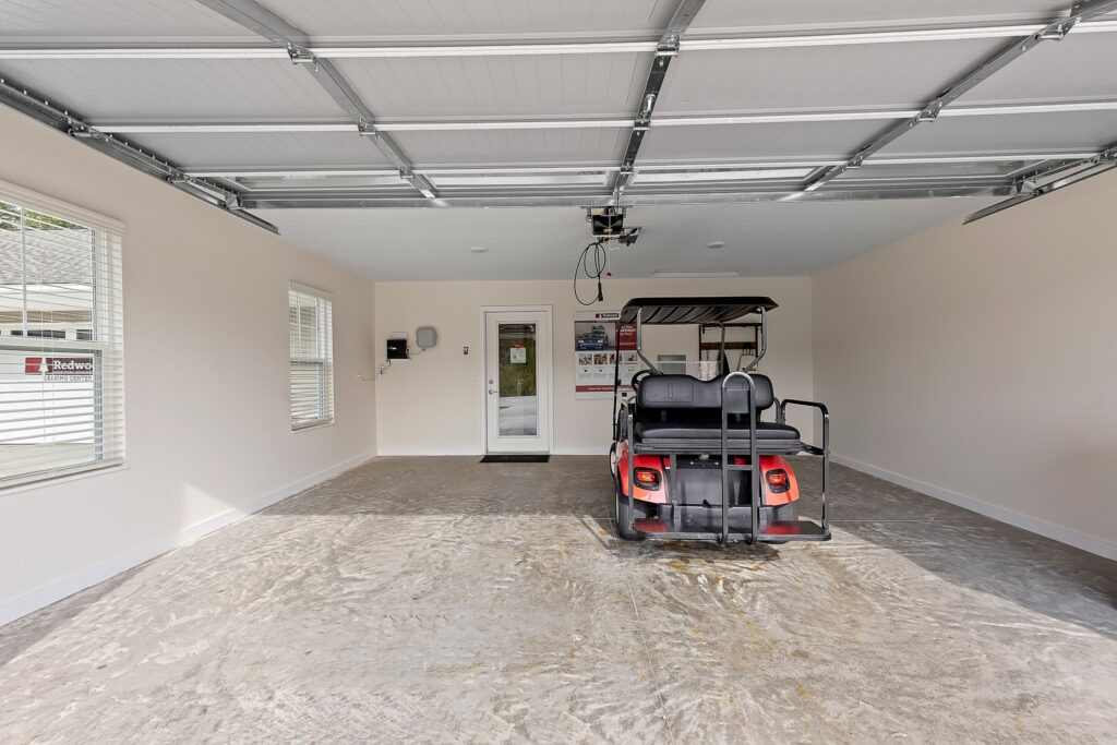 Spacious garage with concrete floor, white walls, open garage door, and a red golf cart parked inside near the back wall.