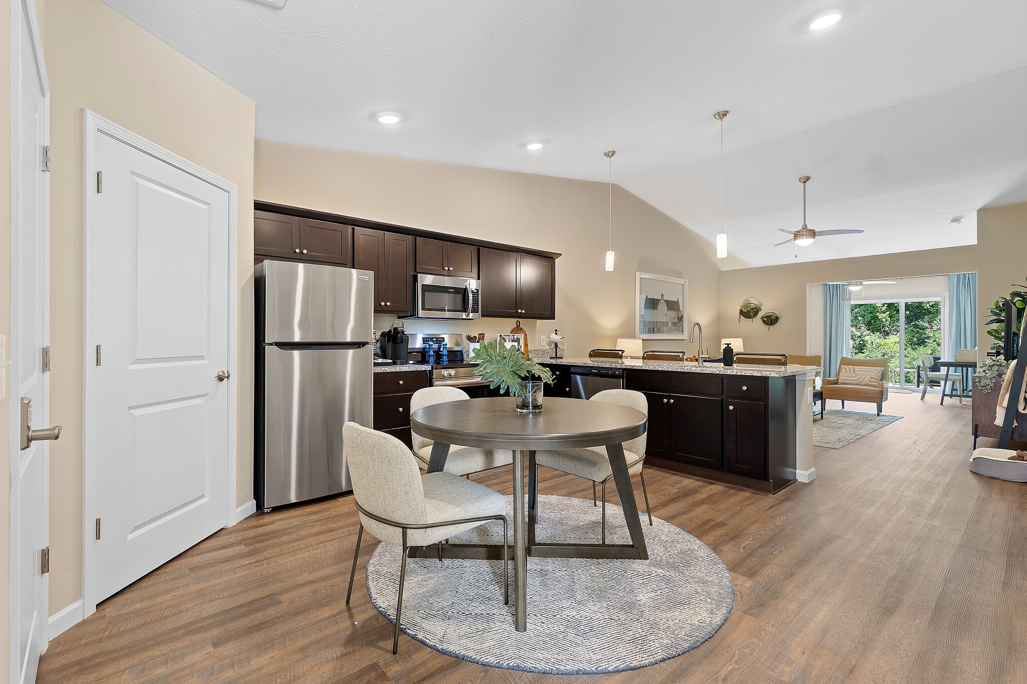 Modern open-concept kitchen and dining area with stainless steel appliances, dark cabinets, round table, and living room visible in the background.