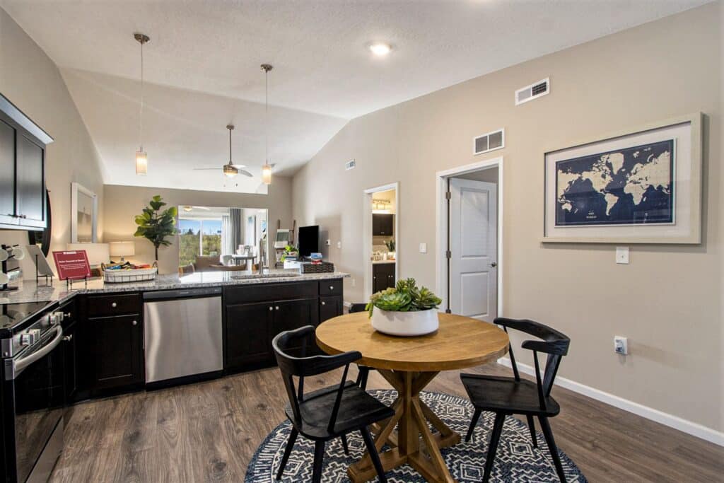Open kitchen and dining area with dark cabinets, stainless steel appliances, round wooden table with four chairs, and a world map artwork on the wall.