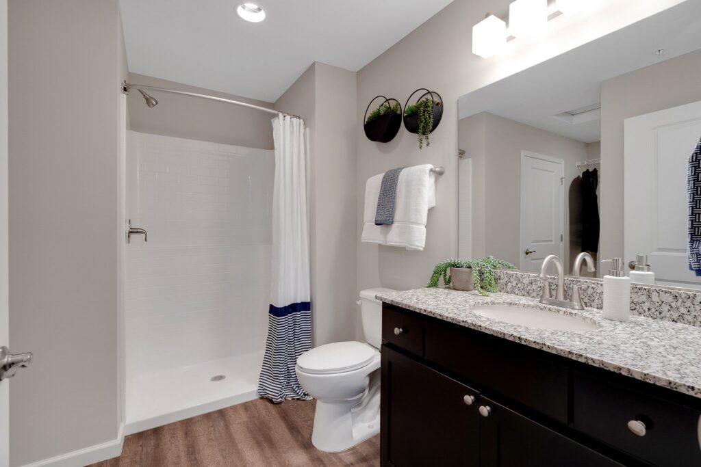 Modern bathroom with a glassless shower, white curtain, toilet, granite countertop vanity, and wall-mounted plants above towel rack.
