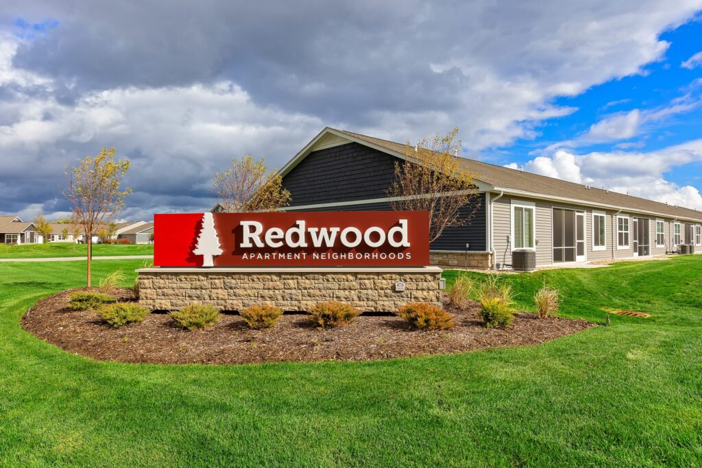 A sign reading "Redwood Apartment Neighborhoods" stands in front of a single-story building surrounded by green grass and landscaping.