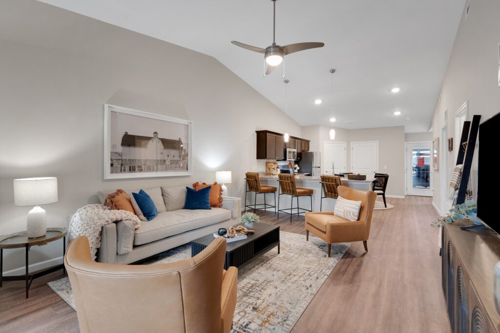 Open-concept living room and kitchen with modern furniture, a sofa, two armchairs, bar stools, neutral decor, and wood flooring.