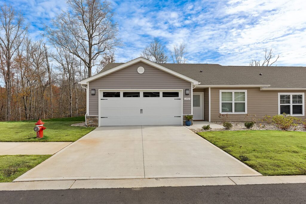 Single-story house with gray siding, white trim, a two-car garage, and a concrete driveway; a red fire hydrant is on the grass near the sidewalk.