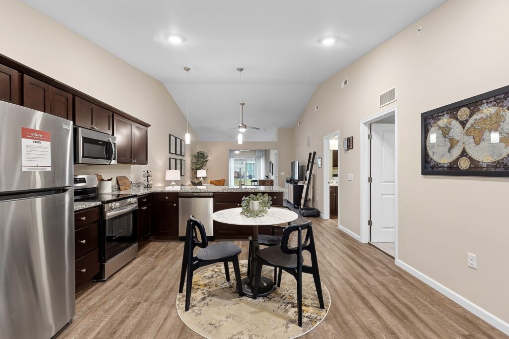 Modern kitchen and dining area with dark wood cabinets, stainless steel appliances, round dining table with four chairs, and wall art on a beige wall.