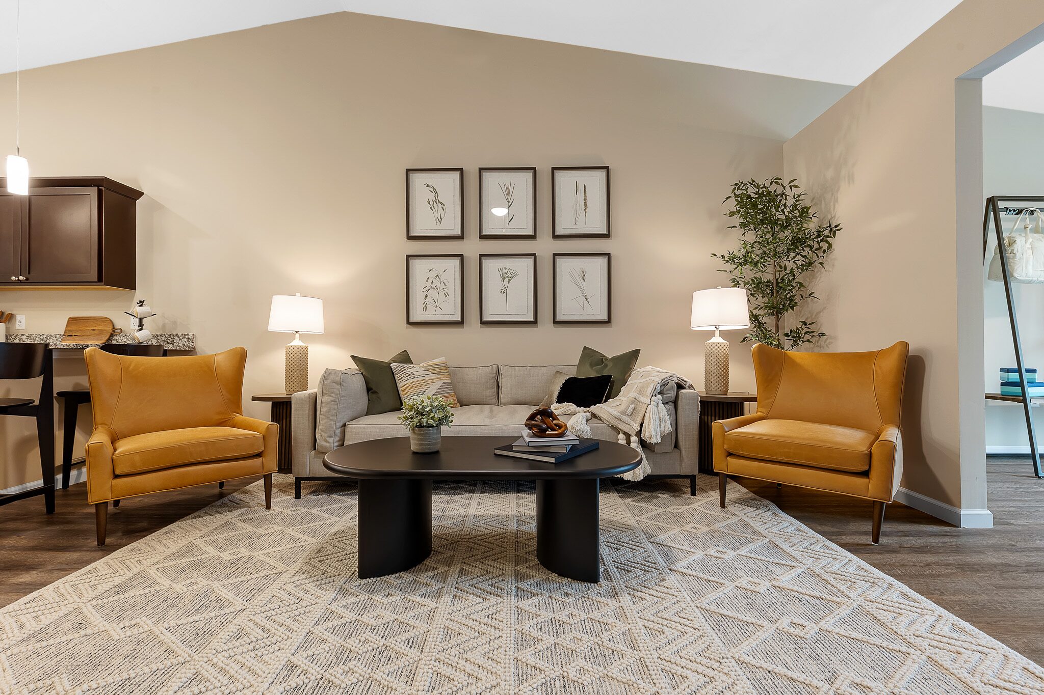 A living room with a gray sofa, two yellow armchairs, a patterned rug, a black coffee table, wall art, two table lamps, and a potted plant in the corner.