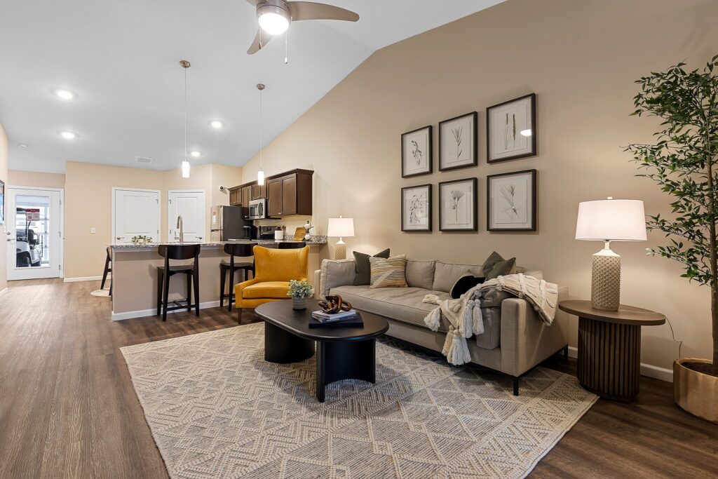 Modern open-concept living room and kitchen with wood flooring, neutral furniture, decorative art on the wall, and warm lighting.