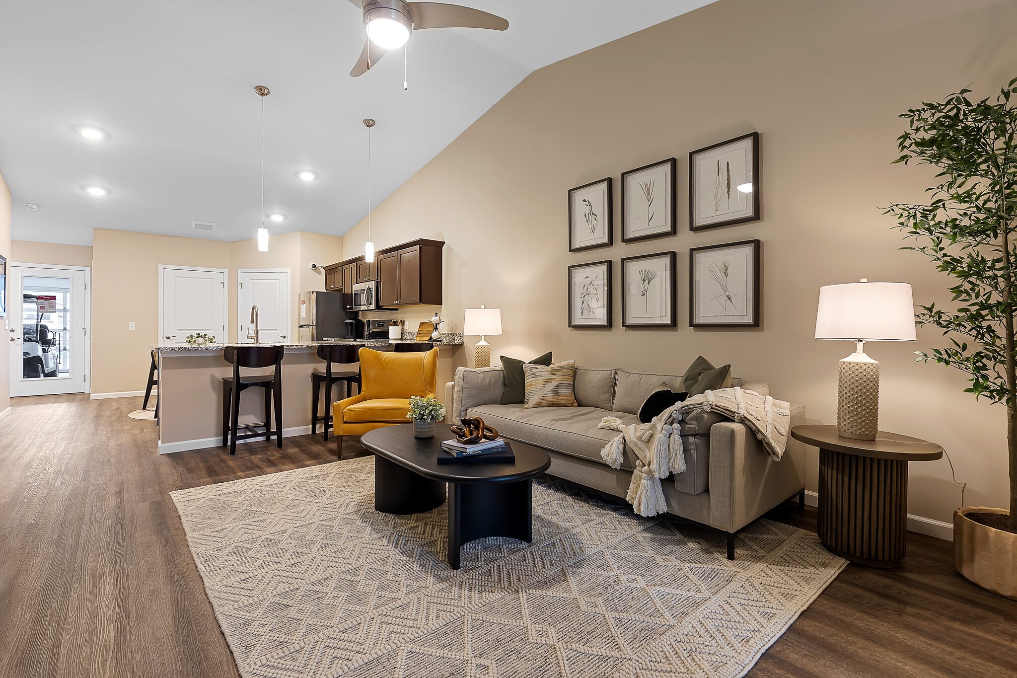 Modern open-concept living room and kitchen with wood flooring, neutral furniture, decorative art on the wall, and warm lighting.