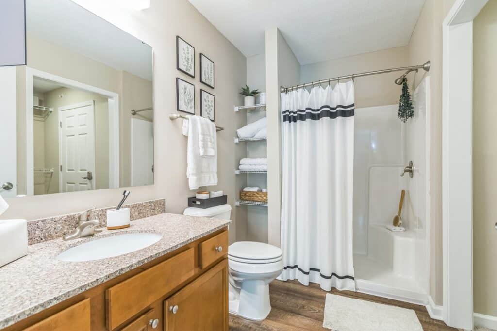 Modern bathroom with a granite countertop, wooden vanity, toilet, walk-in shower with a striped curtain, open shelving with towels, and neutral wall decor.