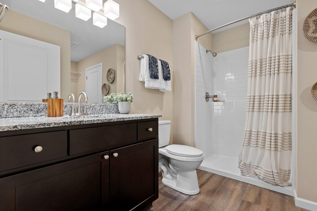 Modern bathroom with dark wood vanity, granite countertop, white toilet, walk-in shower with striped curtain, and neutral-toned walls and decor.
