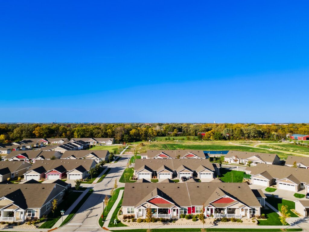 Aerial view of a suburban neighborhood with rows of houses, green lawns, and clear blue sky.