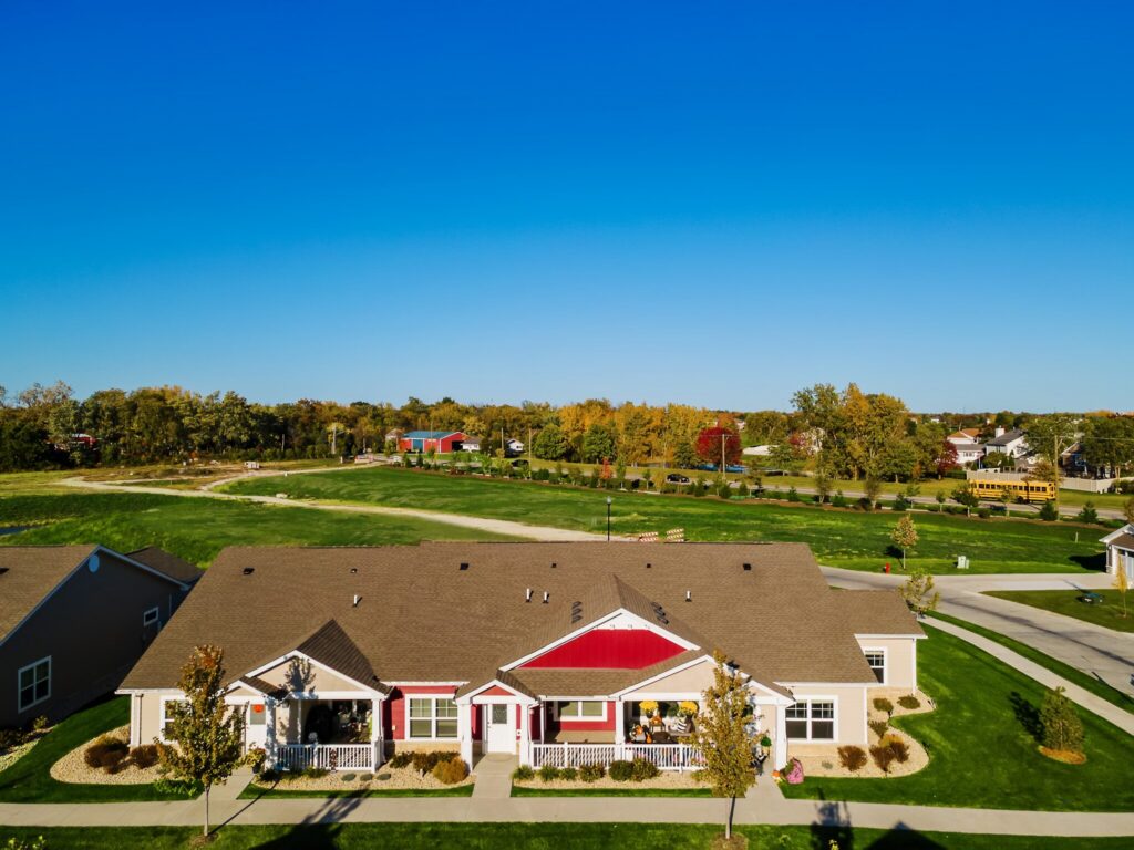 Aerial view of a single-story residential building with a lawn, trees, and a school bus on a road in the background under a clear blue sky.