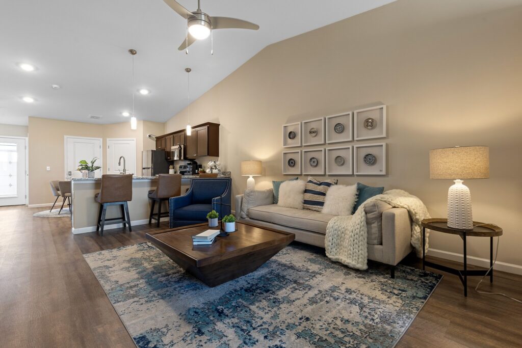 Modern open-concept living room and kitchen with neutral tones, a sectional sofa, contemporary decor, pendant lighting, and a large area rug.