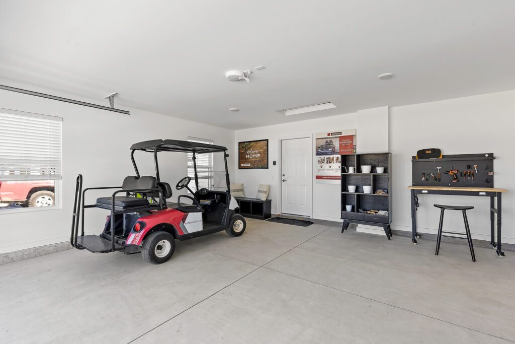 A tidy garage with a red golf cart, a workbench with tools, shelves holding various items, and a door leading into the house.