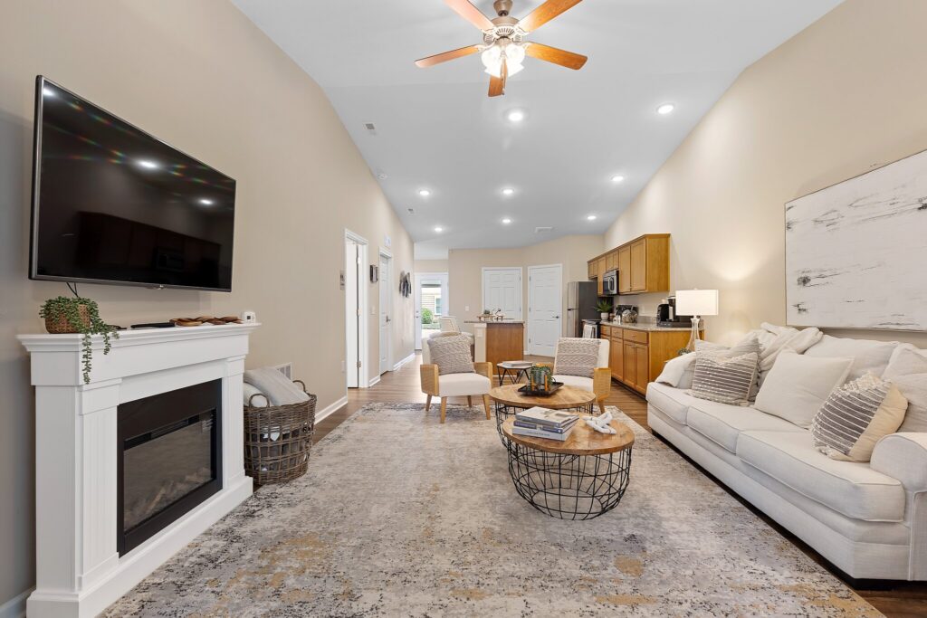 Modern living room with a wall-mounted TV, fireplace, beige sofa, round coffee table, and open kitchen in the background.